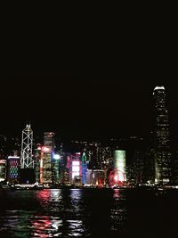 Illuminated buildings by river against sky at night