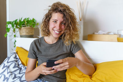 Portrait of smiling woman using mobile phone at home