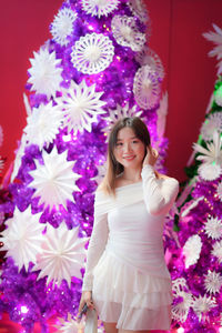 Portrait of young woman standing by christmas tree