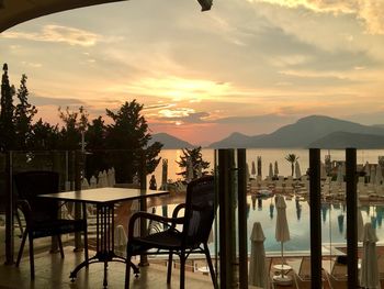 Chairs and table by swimming pool against sky during sunset