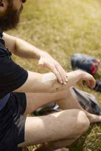 High angle view of man sitting and applying sun cream on his arm