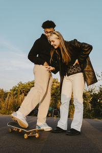 Male and female friends standing by skateboard in park during sunset