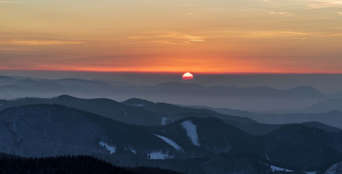 Scenic view of silhouette mountains against orange sky