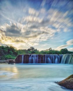 Scenic view of waterfall against cloudy sky