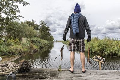 Rear view of man with arms outstretched against lake