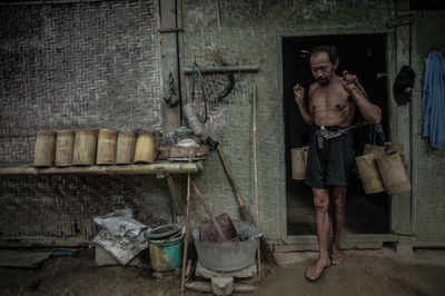 Shirtless man carrying wooden containers while walking at entrance of cottage