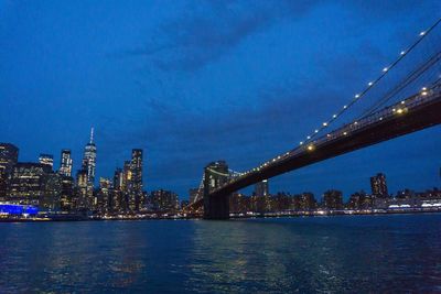 Illuminated bridge over river against sky in city at night