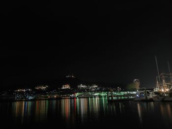 Illuminated buildings by river against sky at night