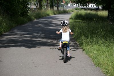 Rear view of boy riding push scooter on road