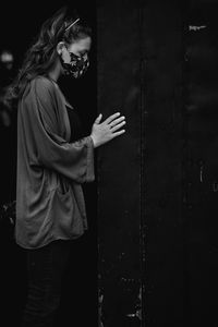 Side view of young woman wearing mask standing against door