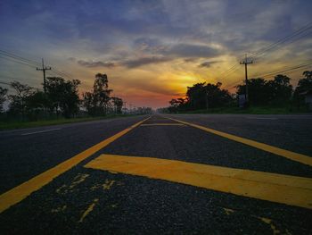 Road by trees against sky during sunset