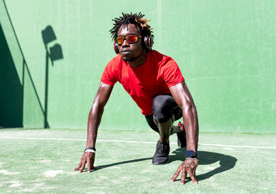 Determined black sportsman with dreadlocks stretching body while warming up before training and listening to music in headphones