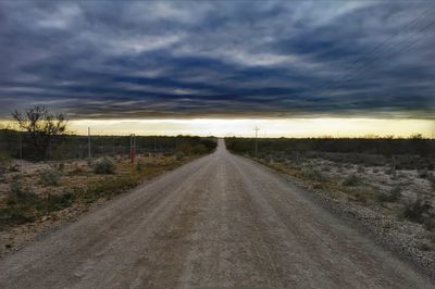 Dirt road amidst field against sky