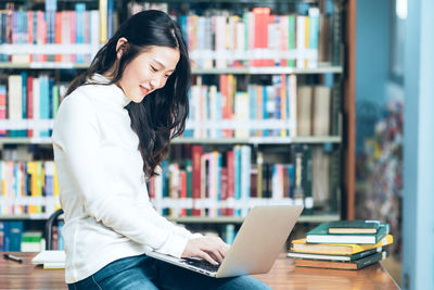 Young woman using phone while sitting on book