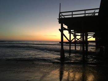Silhouette lifeguard hut on beach against sky during sunset