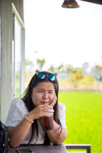  asian woman in a white dress is sucking a soft drink from a straw on a table with a rice field 