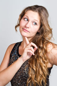 Thoughtful young woman standing with finger on chin against gray background