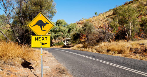 Road sign by trees against sky