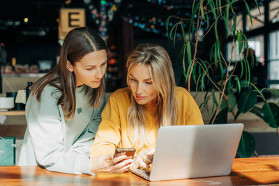 Two business women work behind the counter using electronic gadgets.