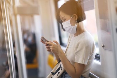 Young woman using phone by window in train