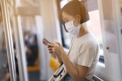 Young woman using phone by window in train