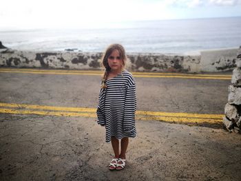 Portrait of girl standing on road against sea