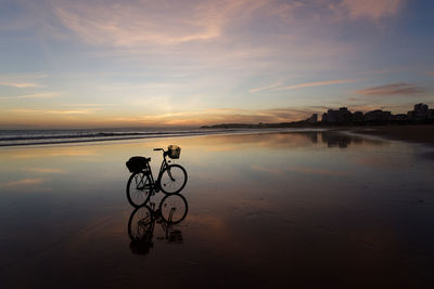 Bicycle on beach against sky during sunset