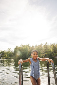 Smiling wet girl holding railing during vacation at lake