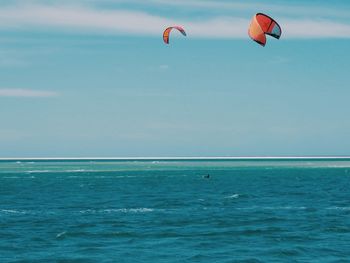 Person paragliding over sea against sky