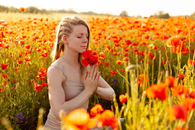 A beautiful girl with closed eyes meditates on a poppy field holding a bouquet of flowers