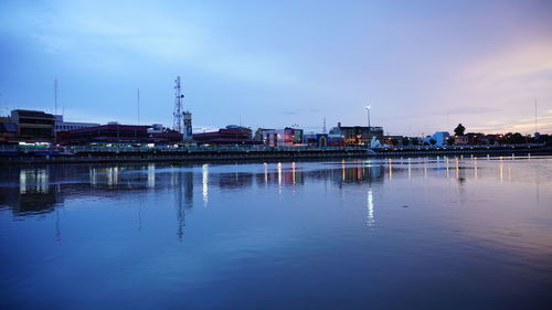 River by illuminated city against sky at dusk