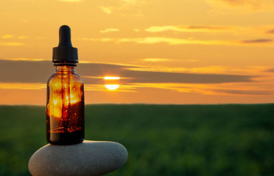 Close-up of glass bottle on field against sky during sunset