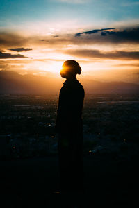 Rear view of silhouette man standing at illuminated sunset