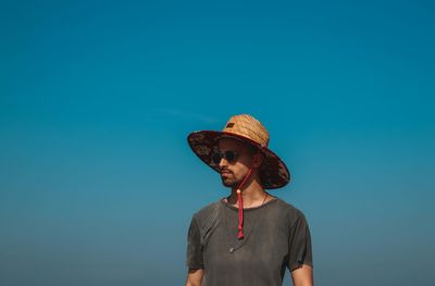 Man wearing hat while standing against clear blue sky