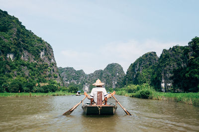 Rear view of man boating in river against sky