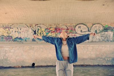 Young woman with arms outstretched standing against graffiti wall