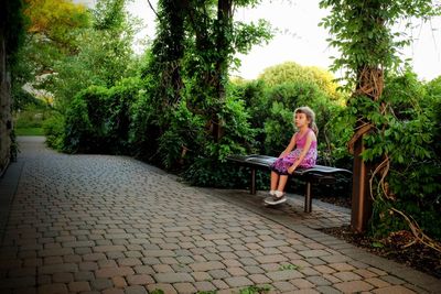 Woman sitting on bench against footpath amidst trees