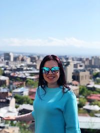 Portrait of woman wearing sunglasses standing against cityscape