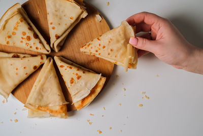 Woman's hand holding delicious crepe, crepes laid out in triangles in a circle on a wooden board