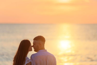 Rear view of couple on sea against sky during sunset