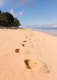 Footprints on sand at beach against sky