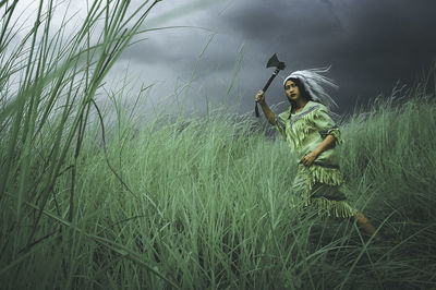 Woman in costume holding axe amidst grass