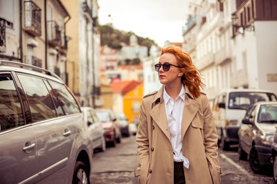 Fashionable young businesswoman standing by cars on street in city