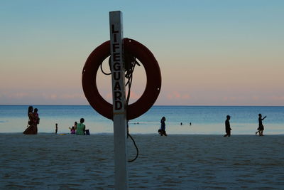 People at beach against sky during sunset