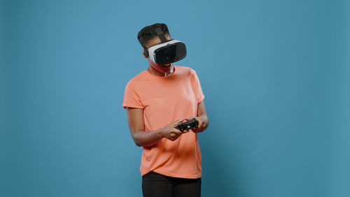 Young woman playing game wearing vr headset against wall