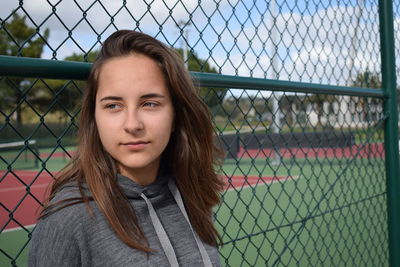 Portrait of beautiful young woman standing by chainlink fence