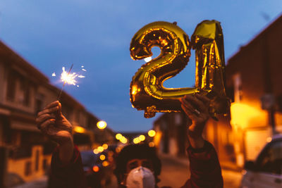 Man holding balloon and sparkler against sky at dusk