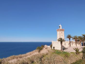 Lighthouse by sea against clear sky