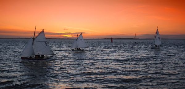 Sailboat sailing on sea against orange sky