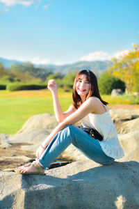 Young woman sitting on field against sky